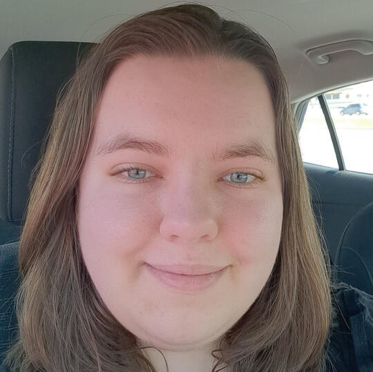 A front facing photo of Caitlin. She is white, has light brown hair, blue eyes, and is smiling.